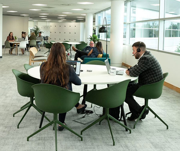 Open-plan-office-area-with-people-sitting-at-round-tables,-having-conversations